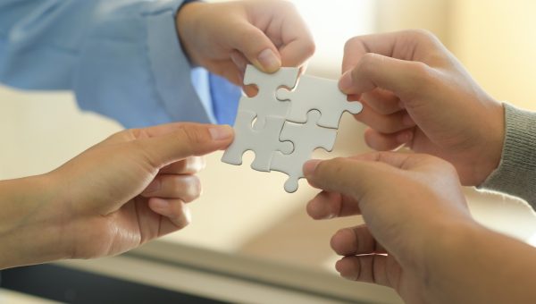 Group of businessmen holding white jigsaw puzzle pieces.