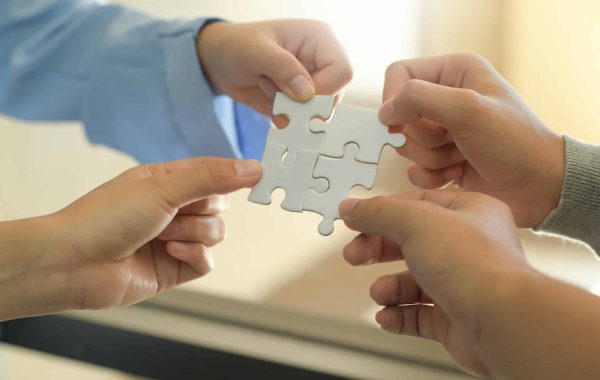Group of businessmen holding white jigsaw puzzle pieces.